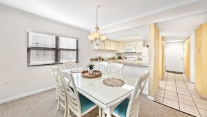 A dining area with a glass table, white chairs, and a chandelier. - Ocean Time Building - Unit #203 (Ocean City)