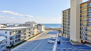 A multi-story parking lot with several cars, a building with balconies, and a view of the beach and ocean. - Ocean Time Building - Unit #203 (Ocean City)
