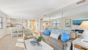 A spacious living room with a large sofa, a dining area, and a kitchen in the background. - Ocean Time Building - Unit #205 (Ocean City)