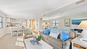 A spacious living room with a large sofa, a dining area, and a kitchen in the background.