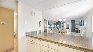 A modern kitchen with granite countertops, a dining area with a glass table, and a living room with a view.