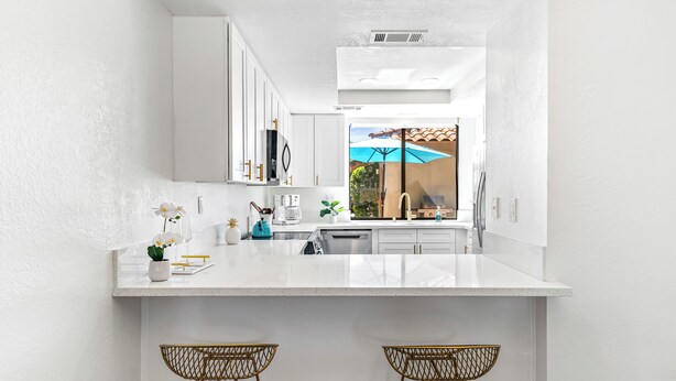 A modern kitchen with white cabinetry, a large island with bar stools, and a view of the outdoors through a window with an umbrella.
