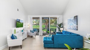 A modern living room with a blue sofa, white armchairs, and a TV on the wall.