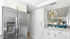 A modern kitchen with white cabinetry, a stainless steel refrigerator, and a unique chandelier.