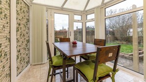 A conservatory with a wooden table and chairs, large windows, and a view of the garden.
