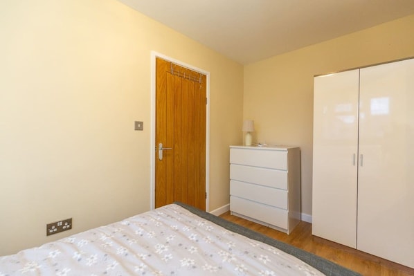 Un dormitorio con una cama, una puerta de madera, un aparador blanco y un armario.