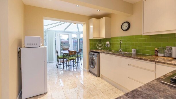 A kitchen with a washing machine, a dining area with chairs, and a clock on the wall.