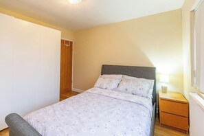 A bedroom with a bed, a nightstand, a lamp, and a wooden wardrobe.