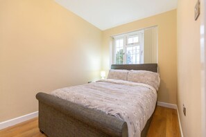 Un dormitorio con cama, mesita de noche, lámpara y ventana.