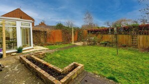 A backyard with a raised garden bed, a wooden fence, and a conservatory.