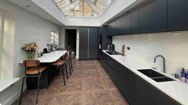 Una cocina moderna con tragaluz, armarios oscuros y una zona de comedor con suelo de madera.