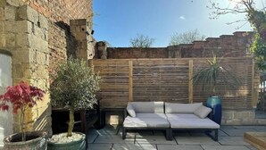 Un espacio al aire libre con un sofá blanco, plantas en macetas y una pared de ladrillo.