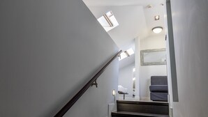 A staircase with dark wooden steps and white walls, leading to a room with a gray chair and a bed. - Tico en Madrid - Ideal Para Parejas (Madrid)