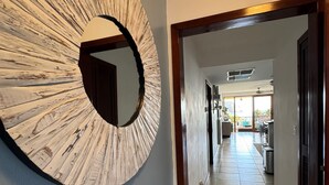 A hallway with a large circular mirror on the wall, a basket of folded blankets, and a view into a dining area with tables and chairs. - San Juan del Sur most exclusive condo! (San Juan del Sur)