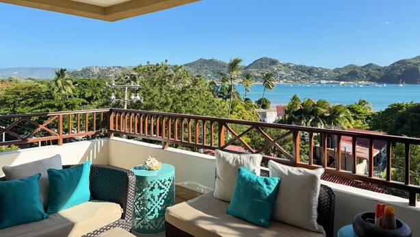 A balcony with a view of the sea and hills, furnished with a sofa and cushions, and a ceiling fan. - San Juan del Sur most exclusive condo! (San Juan del Sur)