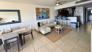 A spacious living room with a sofa, coffee table, and dining area. A kitchen is visible in the background with bar stools. - San Juan del Sur most exclusive condo! (San Juan del Sur)
