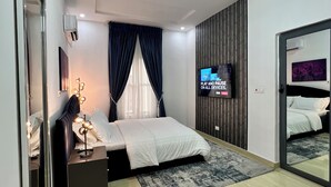 A modern bedroom with a bed, bedside table, mirror, and a TV on the wall.