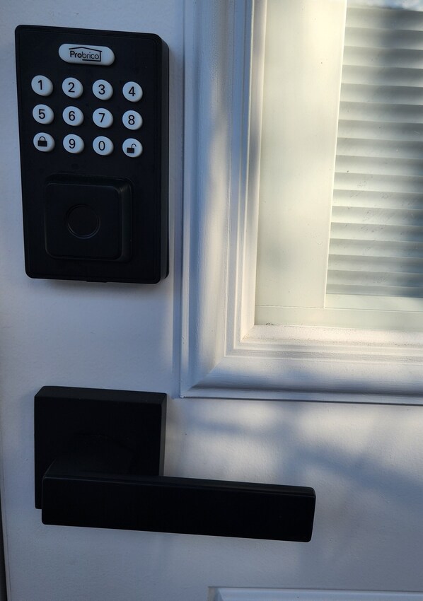 Una puerta con cerradura electrónica, un picaporte y una ventana con persianas.