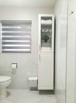 Une salle de bain comprenant des toilettes, un meuble avec des portes en verre et une fenêtre avec des stores.