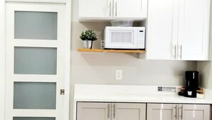 Una cocina con armarios blancos, un microondas, una cafetera y una pequeña planta en maceta sobre una estante.