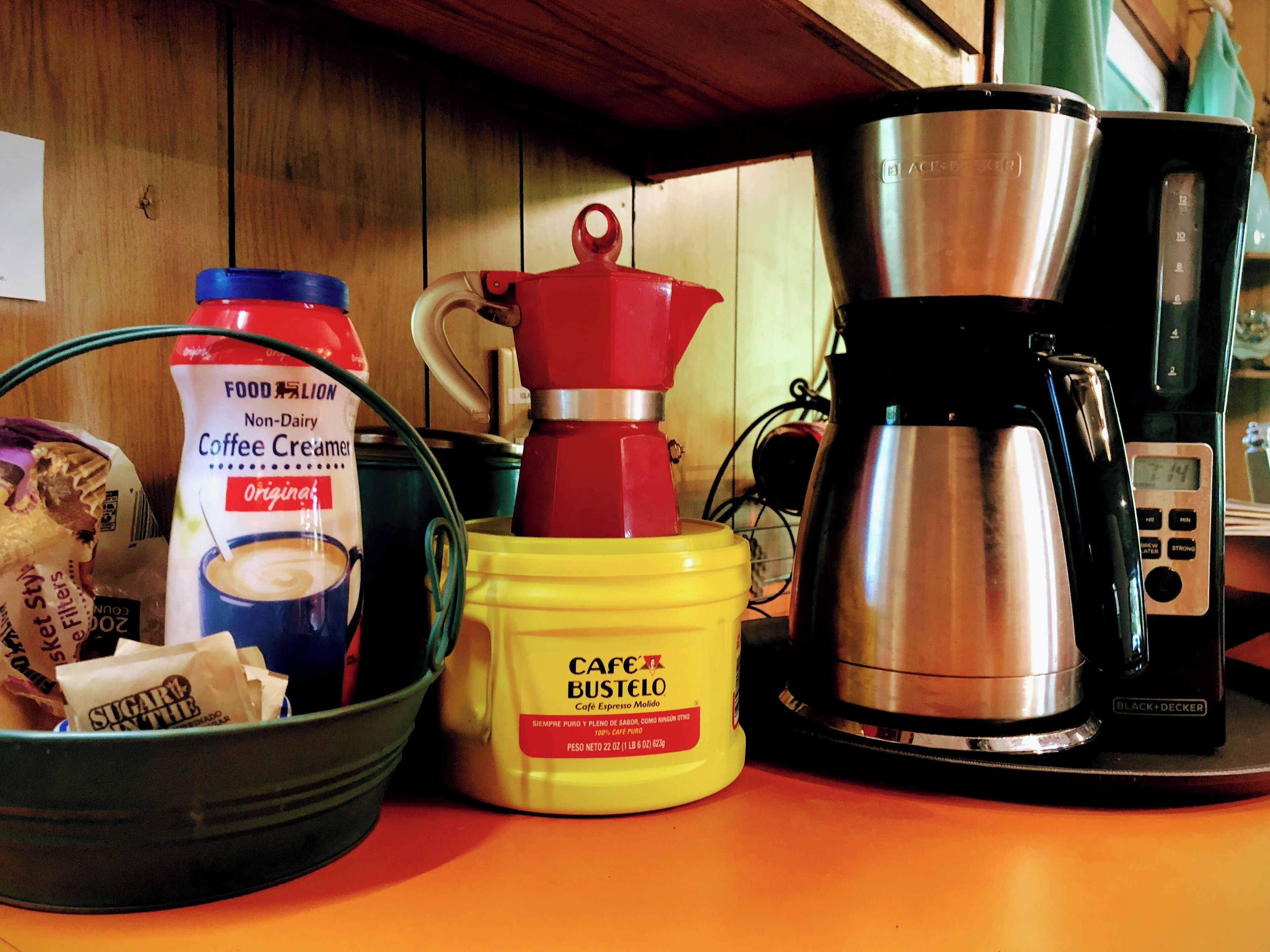 Una encimera de cocina con una cafetera, un envase de leche para café, un sobre de azúcar y un molinillo de café.