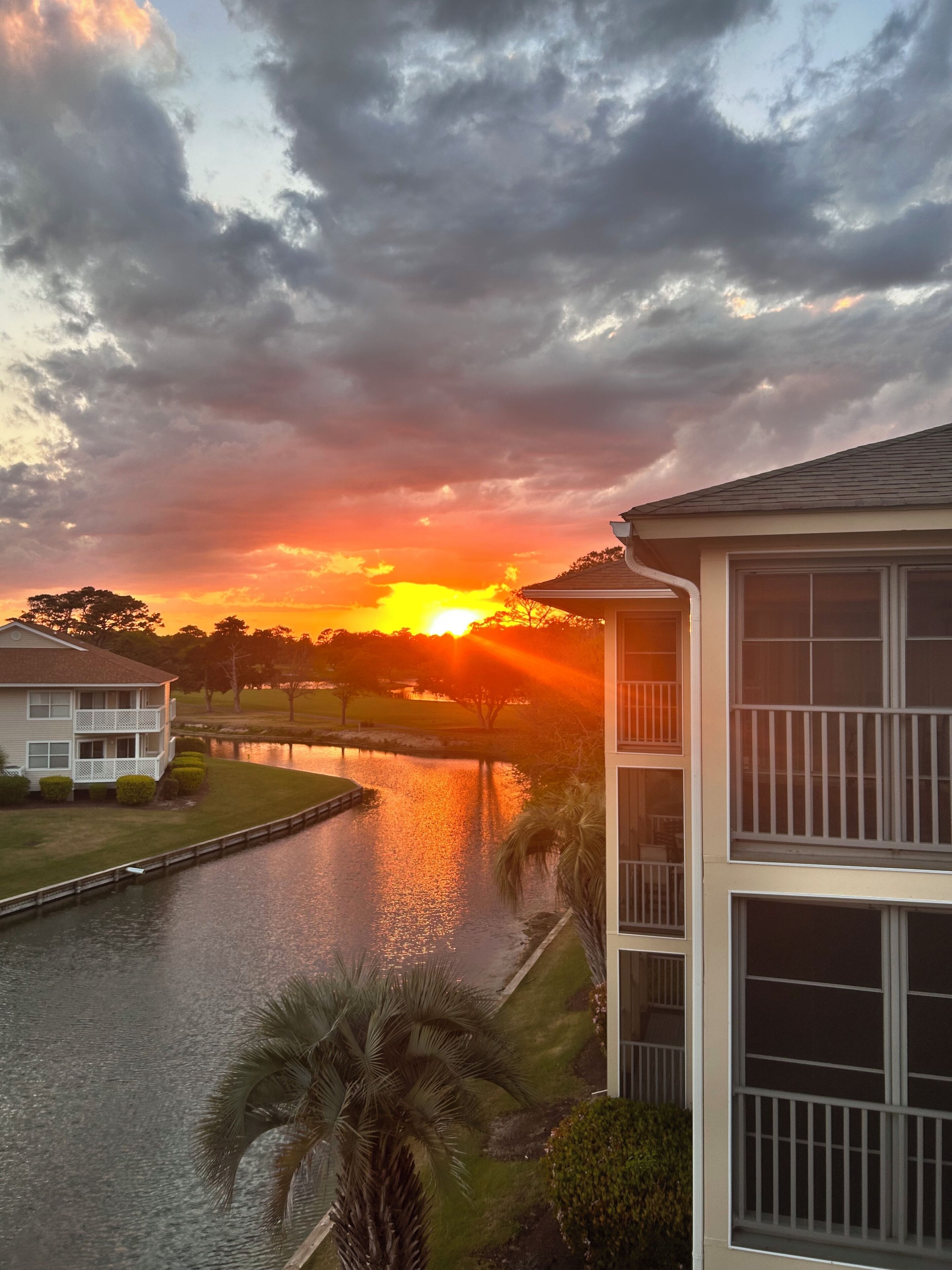 Un edificio residencial con un balcón, una masa de agua y un atardecer de fondo.