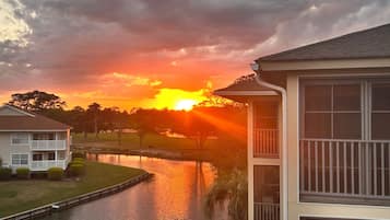 Un edificio residencial con un balcón, una masa de agua y un atardecer de fondo.
