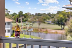 A bottle of wine and two glasses on a balcony railing with a view of a golf course.