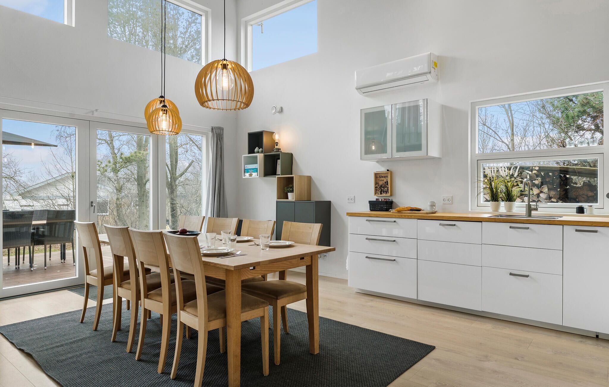 A modern kitchen with white cabinets, a wooden dining table, and pendant lights.
