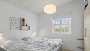 Een slaapkamer met een bed, een raam, een wandplank met decoratieve objecten en een hanglamp.