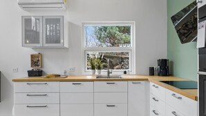 Een moderne keuken met witte kastjes, een houten aanrecht, een raam met uitzicht op bomen en een koffiezetapparaat.