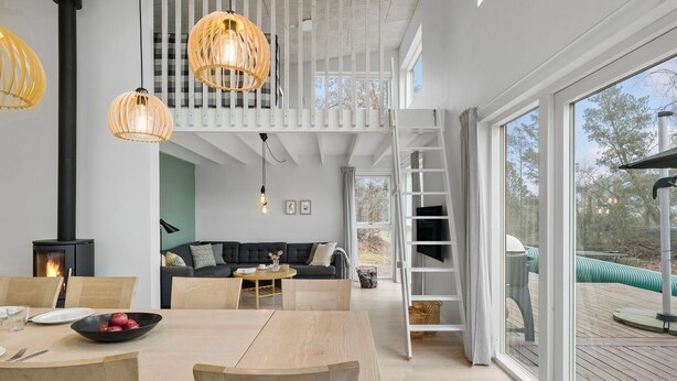 Een modern interieur met een eethoek, een bank, een open haard en een groot raam met uitzicht op de omgeving.