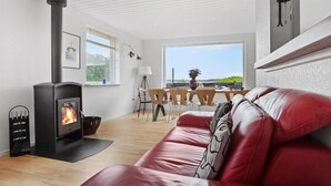 A modern living room with a fireplace, a red leather sofa, wooden flooring, and a view of the sea through large windows. - 4 bedroom gorgeous home in Gråsten (Gråsten)