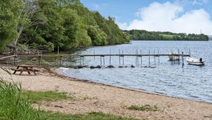 A lakeside picnic area with a dock extending into the water, a boat moored at the dock, and a picnic table on the sandy shore. - 4 bedroom gorgeous home in Gråsten (Gråsten)