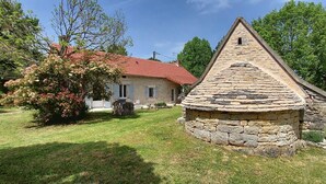 Un edificio de piedra con techo de tejas rojas, un pequeño jardín y un árbol.