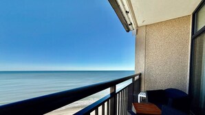 Een balkon met uitzicht op zee, een tafeltje en een stoel.