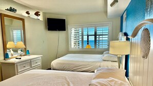 Een hotelkamer met twee bedden, een grote spiegel, een televisietoestel en een raam met luxaflex.
