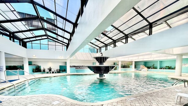 An indoor swimming pool with a central fountain, surrounded by tiled flooring and glass ceiling. - King bed studio amenities 812 (Myrtle Beach)