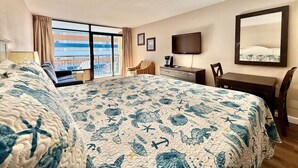 A hotel room with a large bed, a desk, a chair, a TV, and a balcony with a view. - King bed studio amenities 812 (Myrtle Beach)