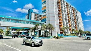 A multi-story hotel with a modern design, featuring balconies on each floor, a parking area in front, and a clear blue sky. - King bed studio amenities 812 (Myrtle Beach)