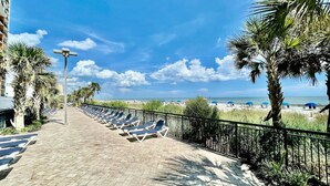 A paved walkway with sun loungers and palm trees, leading to a beach. - King bed studio amenities 812 (Myrtle Beach)