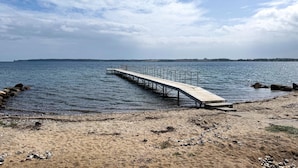 A wooden pier extending into calm water, surrounded by a sandy beach with scattered rocks. - Gorgeous home in Juelsminde with sauna (Juelsminde)
