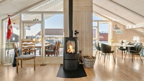 A spacious loft with a large black wood-burning stove, wooden floors, and a dining area with modern furniture. - Gorgeous home in Juelsminde with sauna (Juelsminde)