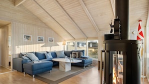 A spacious living room with a large blue sectional sofa, a round coffee table, and a wood-burning stove. - Gorgeous home in Juelsminde with sauna (Juelsminde)