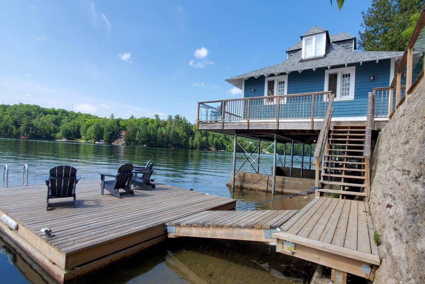 Una cabana a la vora d'un llac amb un moll, dues cadires Adirondack i una terrassa coberta.