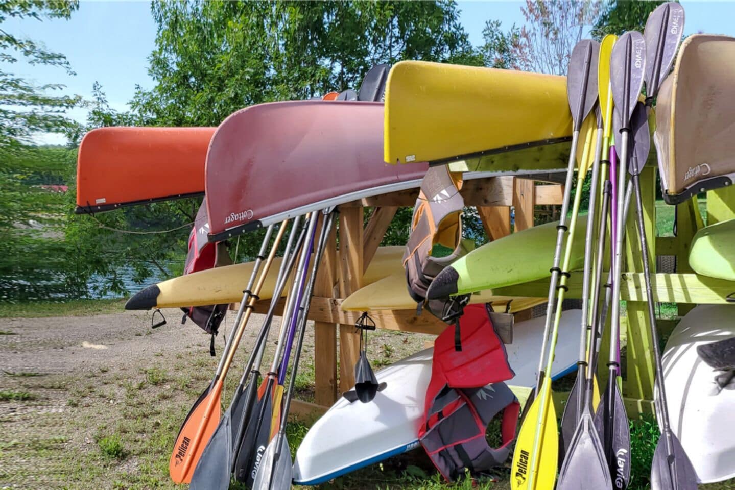 A collection of canoes and kayaks of various colors, including red, yellow, green, and white, leaning against a wooden structure.