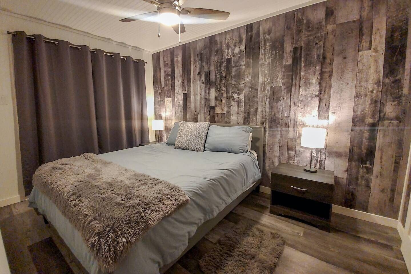 A bedroom with a bed, two bedside tables, a ceiling fan, and wooden panel walls.