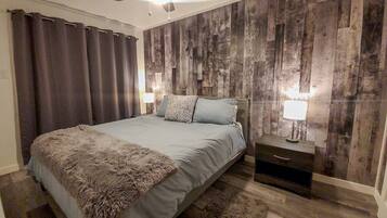 A bedroom with a bed, two bedside tables, a ceiling fan, and wooden panel walls.