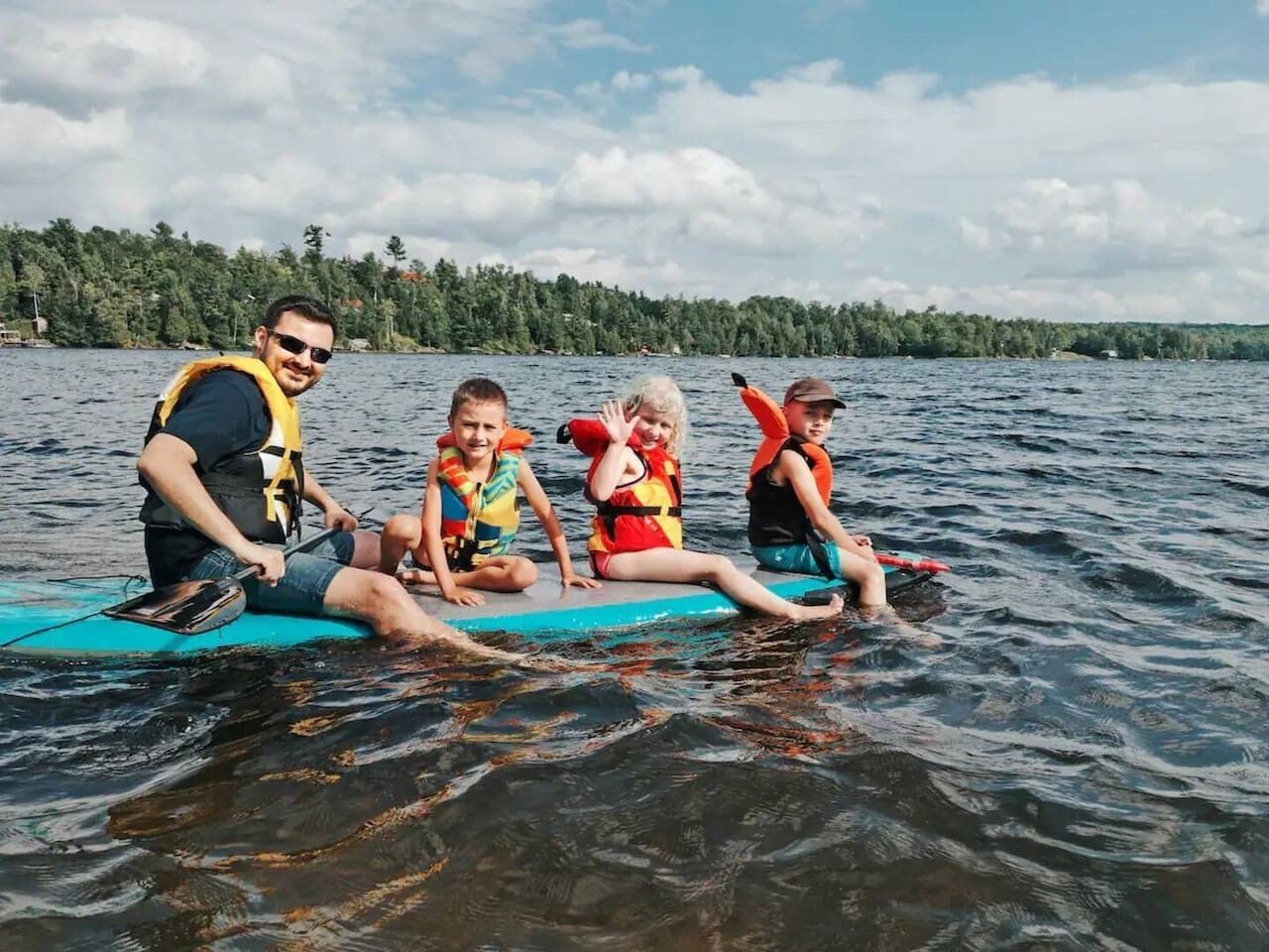 A group of people on a paddleboard in a lake with trees in the background.