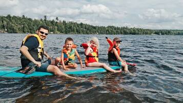 A group of people on a paddleboard in a lake with trees in the background.